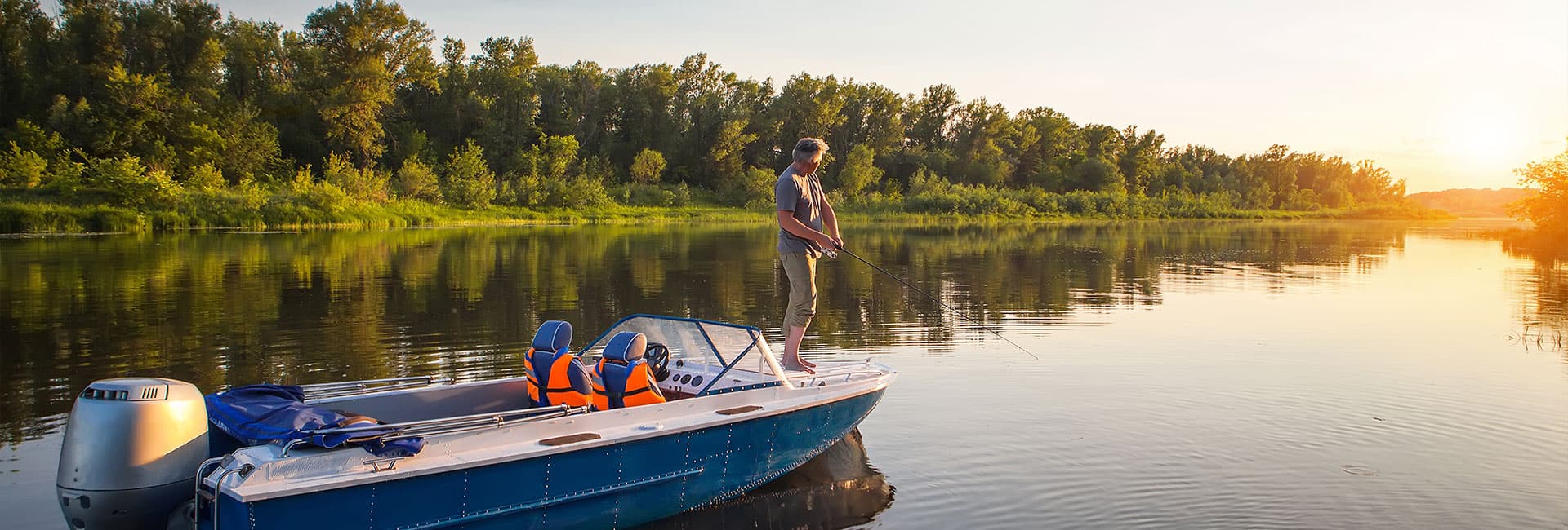 A person fishing from a small boat on a calm river at sunset.