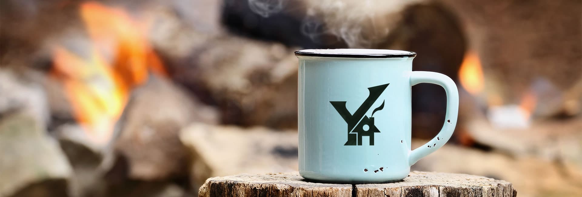 A steaming light blue mug sits on a wooden stump with a fire in the background.