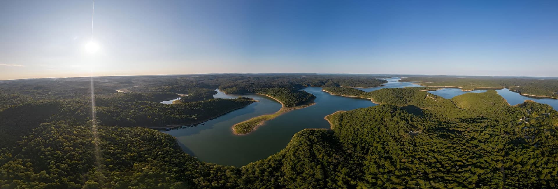 A panoramic aerial view of lush green hills and winding waterways under a clear blue sky.