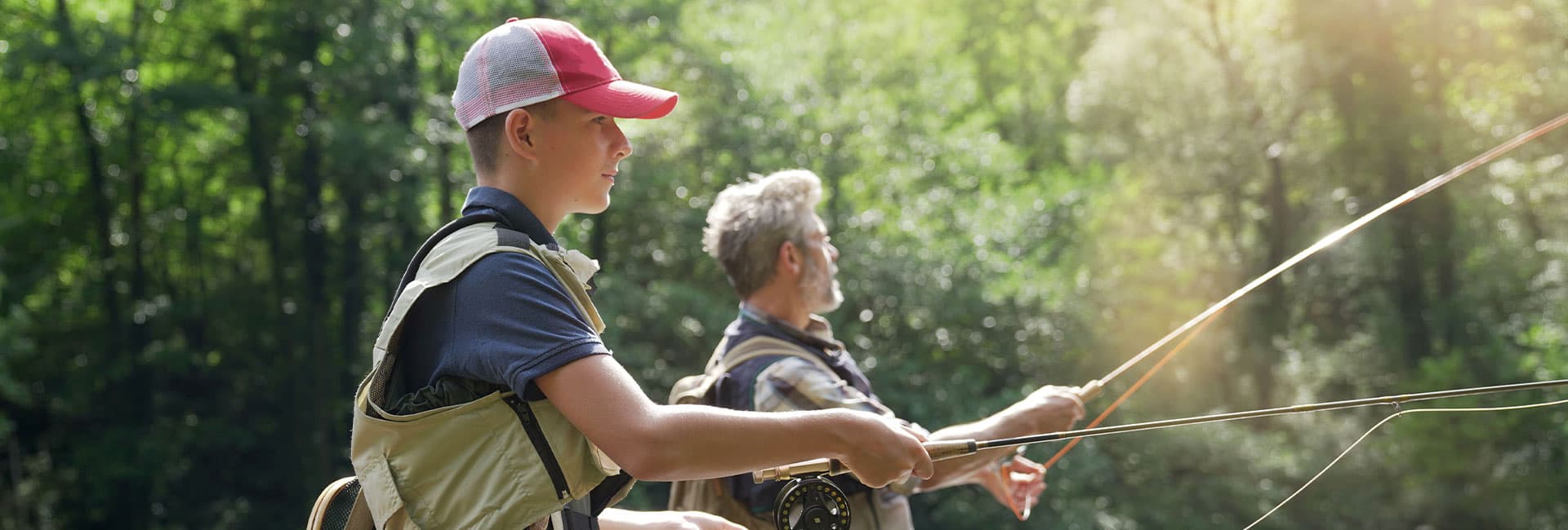 Two people fishing together in a lush, green outdoor setting.